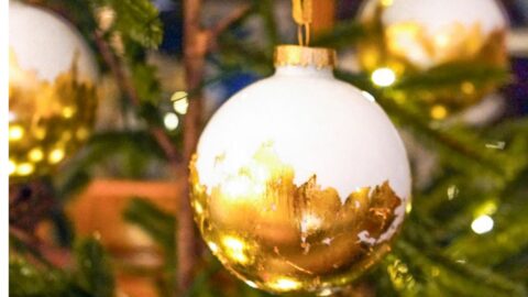 A close-up of a Christmas tree adorned with elegant gold leaf ornaments accentuated in white and gold. These intricate decorations, paired with twinkling lights, create a warm and festive atmosphere.