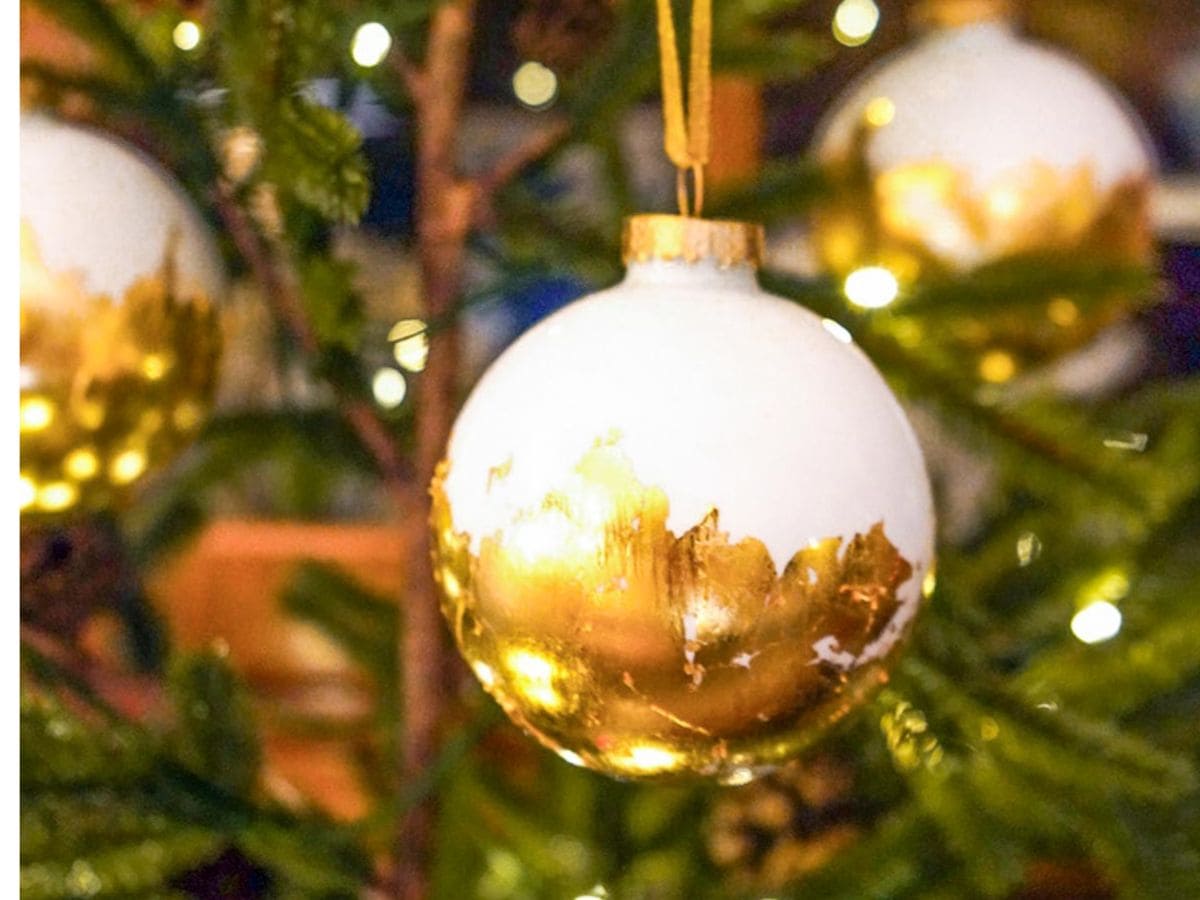 A close-up of a Christmas tree adorned with elegant gold leaf ornaments accentuated in white and gold. These intricate decorations, paired with twinkling lights, create a warm and festive atmosphere.