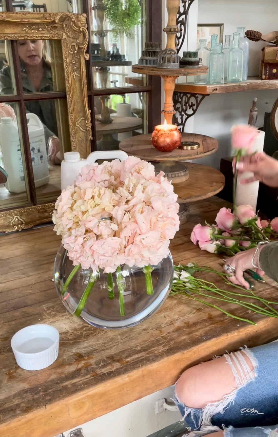 basic floral arrangement in a short, round glass vase filled with pink hydrangeas and pink roses.