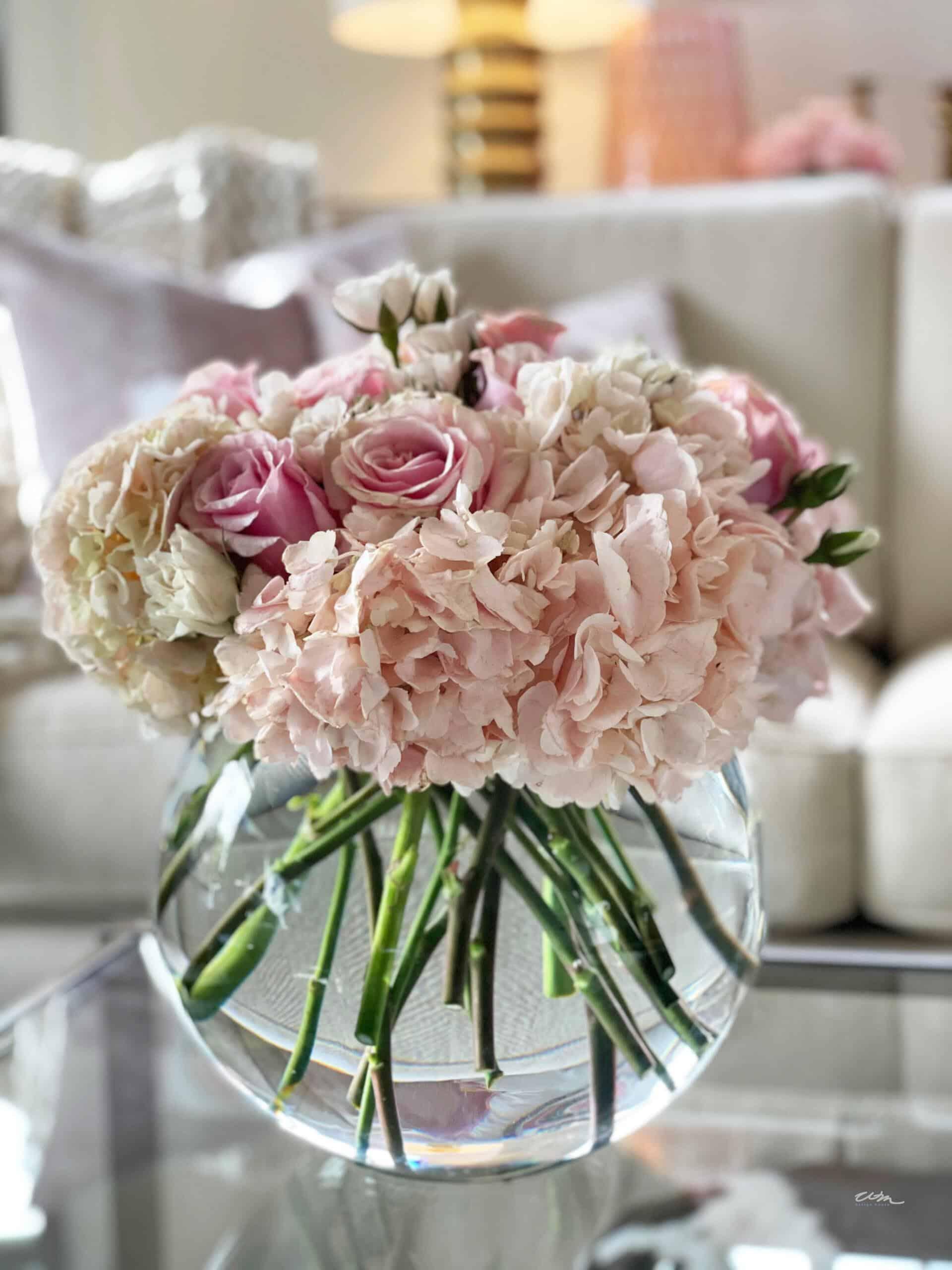 basic floral arrangement in a short, round glass vase filled with pink hydrangeas and pink roses.