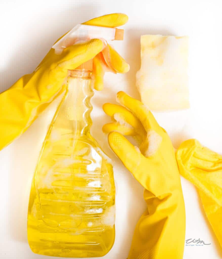 hand in yellow glove holding a bottle of cleaner