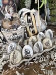 Decorative eggs with black feather designs are displayed in a carton and a pot, surrounded by shredded paper and rustic decor, making for unique adult Easter egg ideas. A charming tag labeled "EGG" completes this stylish arrangement.