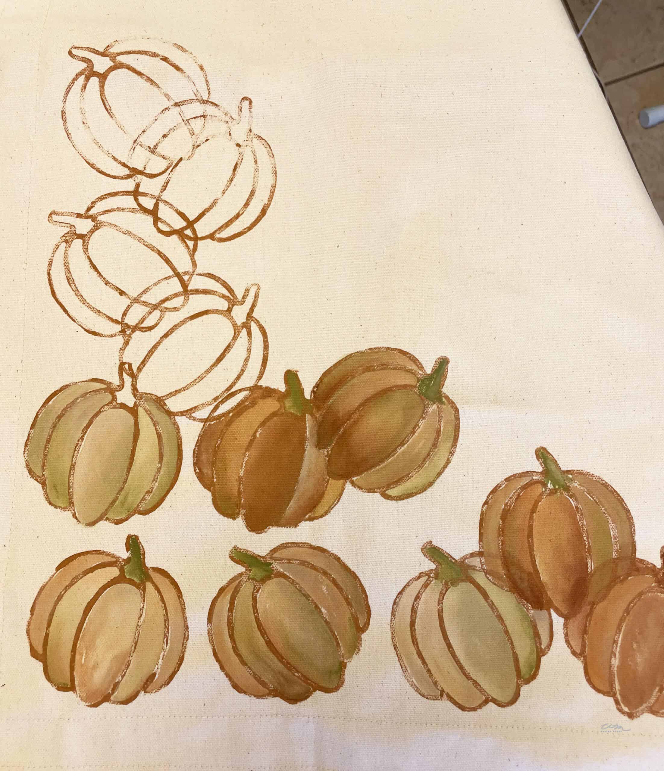 A cream-colored cloth featuring a pattern of 10 pumpkins, perfect for a fall throw pillow. The pumpkins are illustrated in various shades of brown and green, with some in outline form while others are shaded in. The design is clustered towards the corner of the fabric.