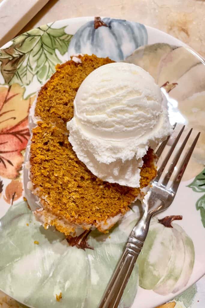 An image of a  piece of pumpkin bundt cake on a plate with a scoop of vanilla ice cream. 