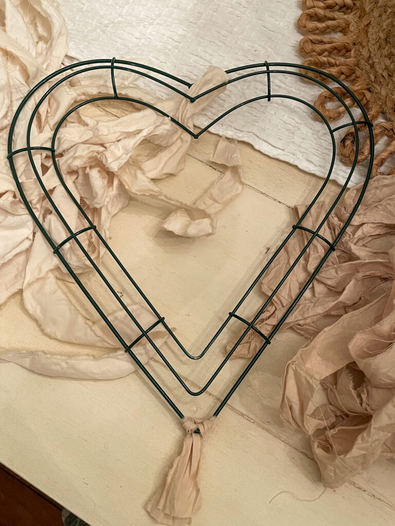 To assemble your Valentine's Day Wreath, take a fabric strip, fold in half, and place the loop end of the fabric under the wire and up the other side. Then, put the two end pieces through the loop and pull.