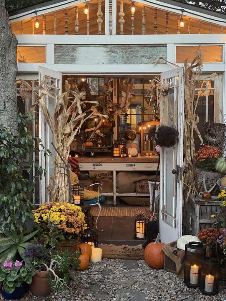 The she shed in the fall decorated for Halloween with pumpkins, mums, lantern, and DIY Halloween crafts 