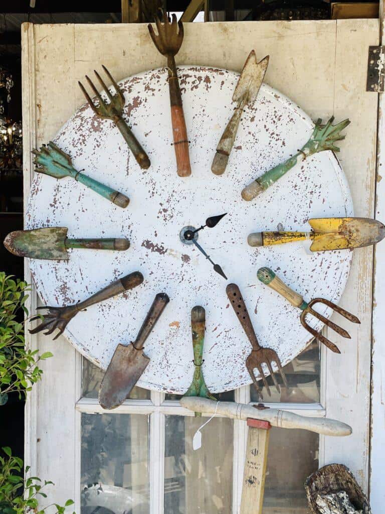 Beautiful DIY outdoor wall clock made from an oil drum lid and gardening tools.