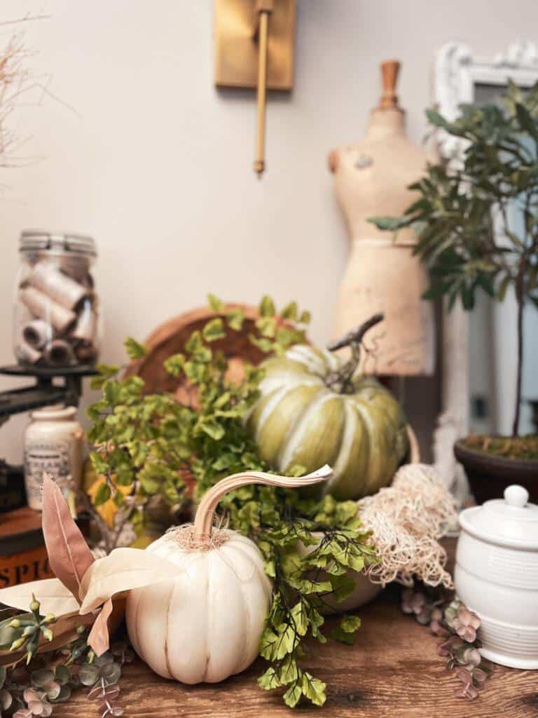 Vignette with green and white pumpkins on a side table with a vintage manequin. 