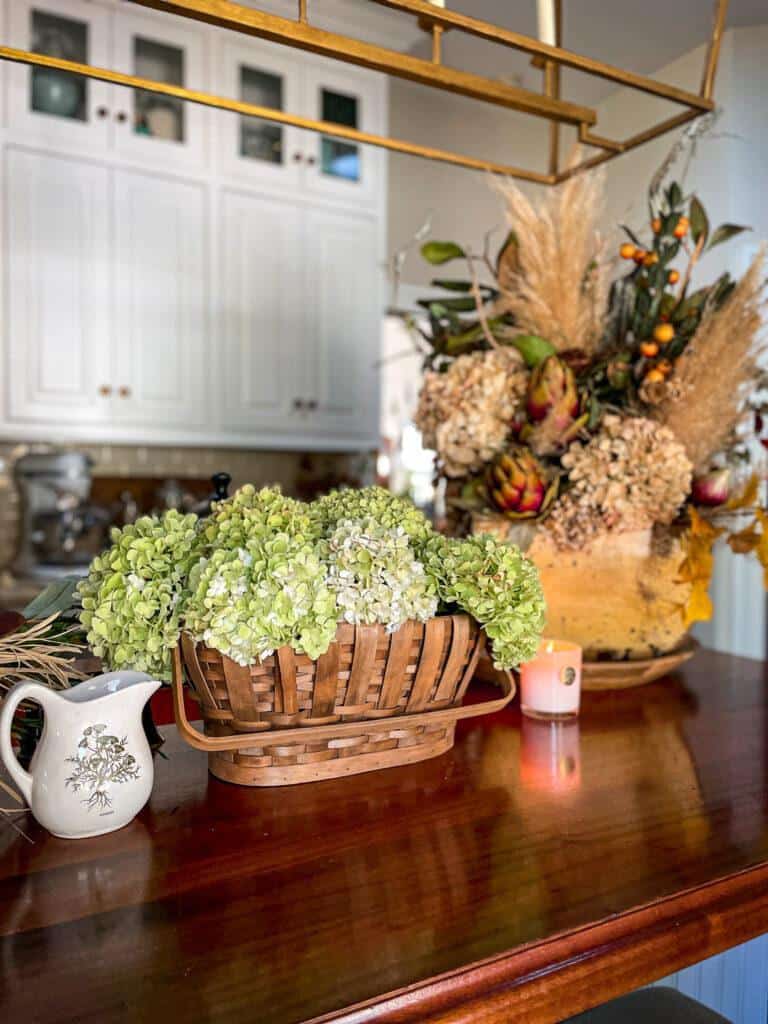 Fall vignette styled on the kitchen counter with green hydrangeas, a candle and a floral arrangement full of dried flowers. 