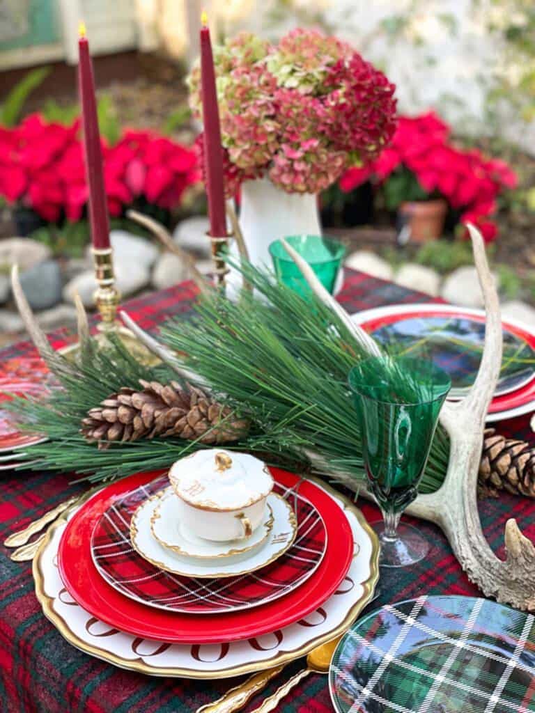 Christmas tablescape with plaid plates, blue and white dishes, greenery and antlers.