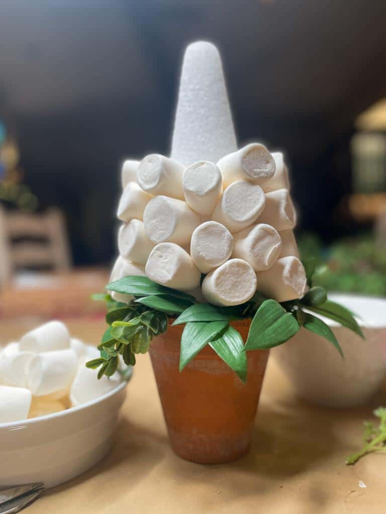 process of adding marshamllows to a styrofoam tree to create a small white christmas tree out of marshmallows 