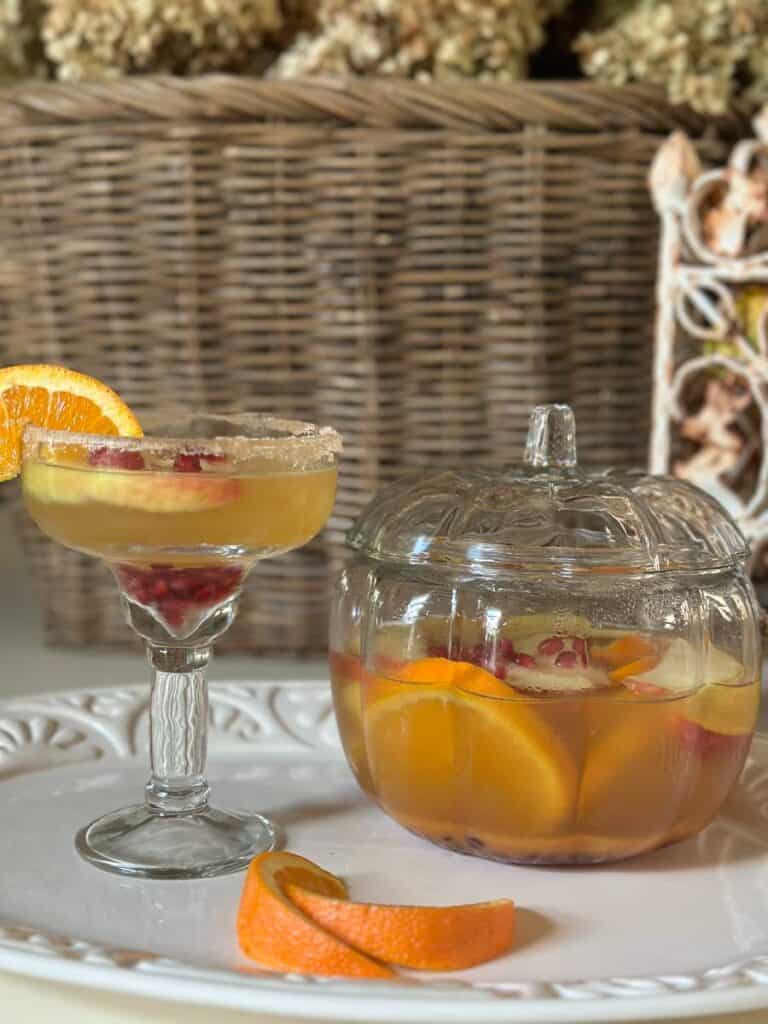 Pumpkin-shaped glass container with sangria sitting next to a glass of sangria on a table. 