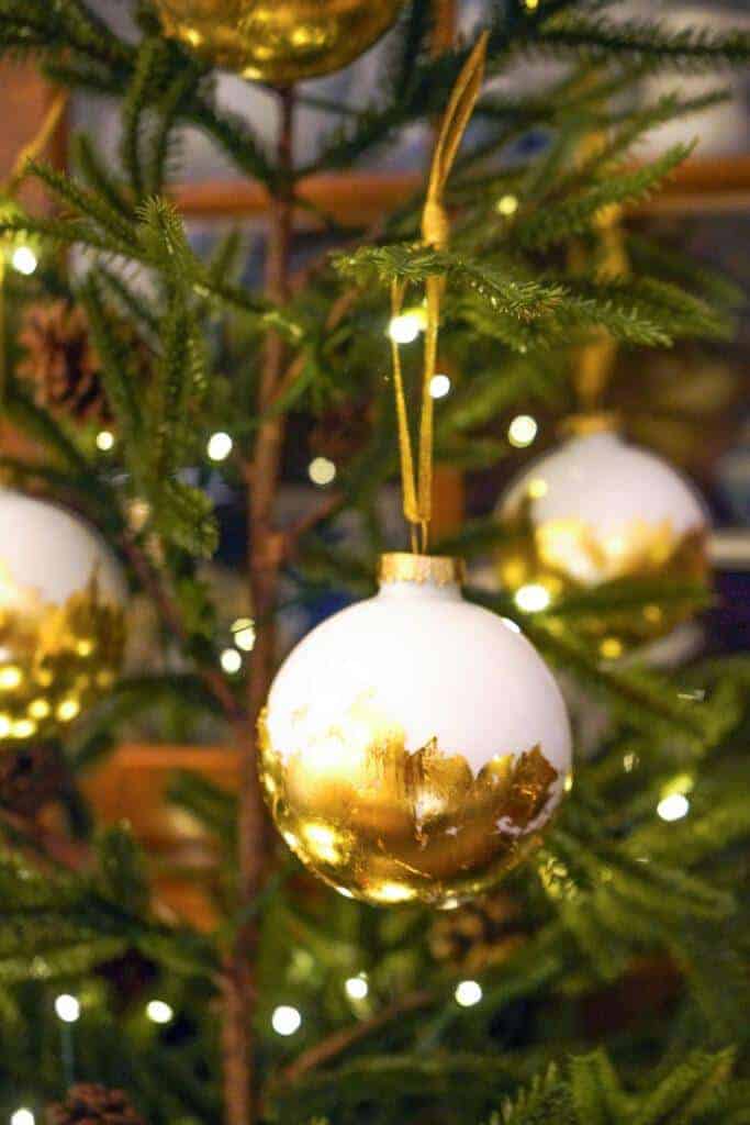 Gold and white foiled ornaments are hanging on the Christmas tree. 