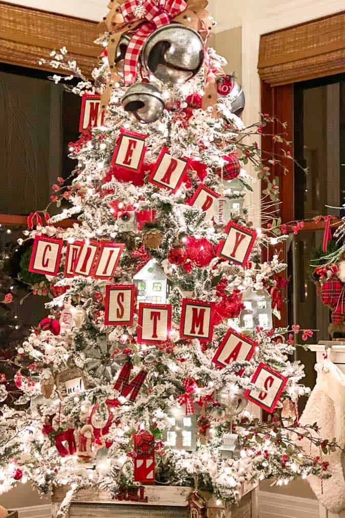 White frosted Christmas tree decorated with giant bells and a merry Christmas banner 