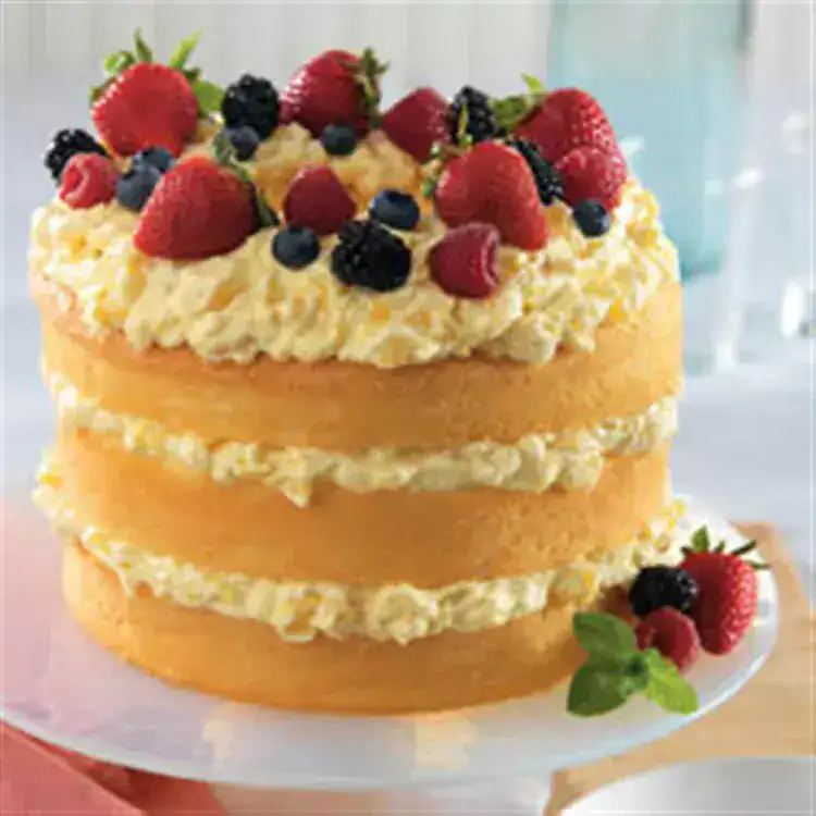 Three-layer yellow cake made with store-bought angel food cake mix and creamy pineapple filling between layers, topped with whipped cream and assorted fresh berries, including strawberries, raspberries, blackberries, and blueberries, garnished with mint leaves.