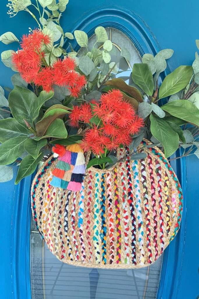 How To Make 27 Unique Summer Front Door wreaths And More-A colorful straw bag filled with flowers hanging on the front door.