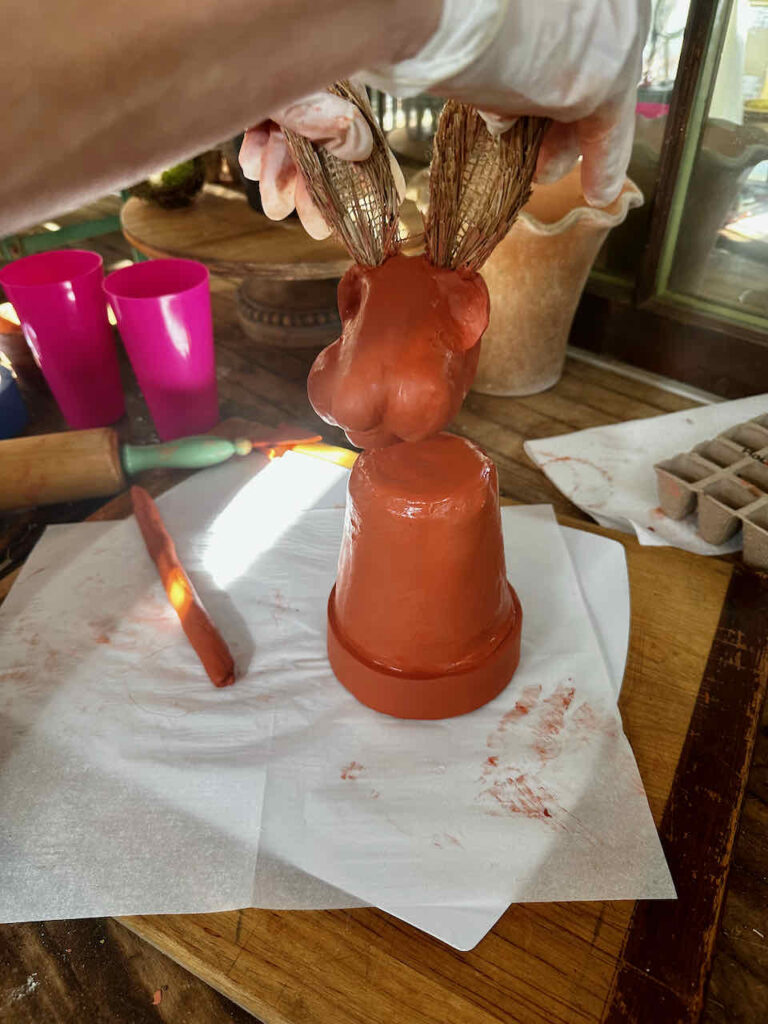 Attaching the red clay rabbit head to the top of a flower pot that is also covered in red clay 