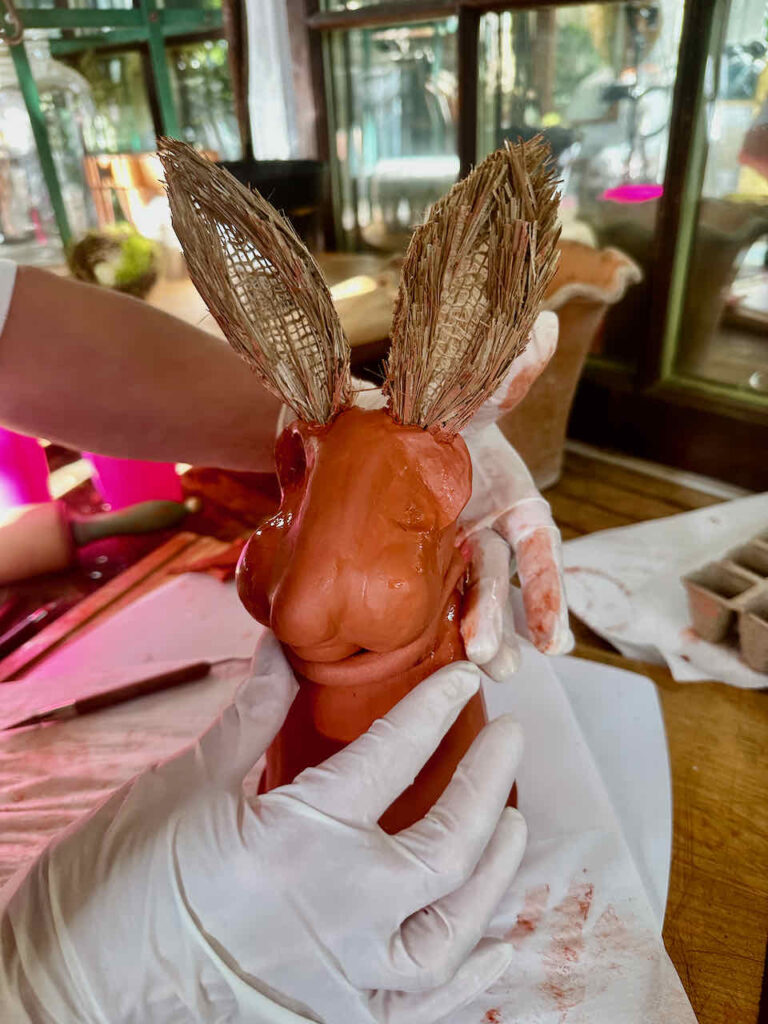Attaching the red clay rabbit head to the top of a flower pot that is also covered in red clay