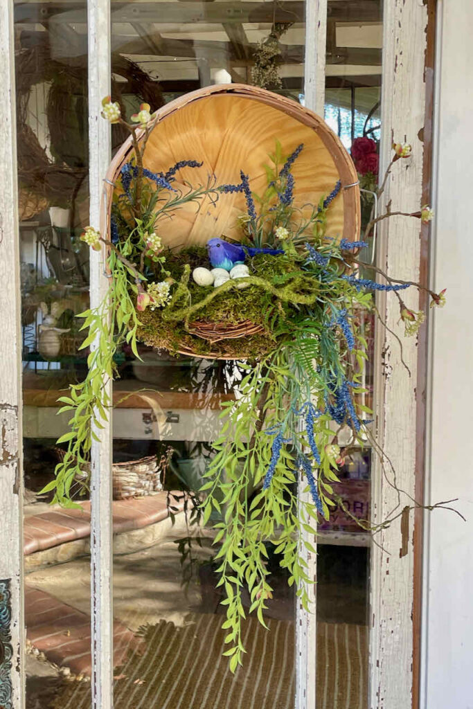 How To Make 27 Unique Summer Front Door wreaths And More-a bushel basket hanging on a door with a birds nest and greenery.