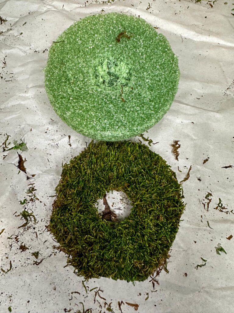 In process picture of DIY moss mushroom. Styrofoam ball cut in half for the cap of the mushroom showing how to attach moss.