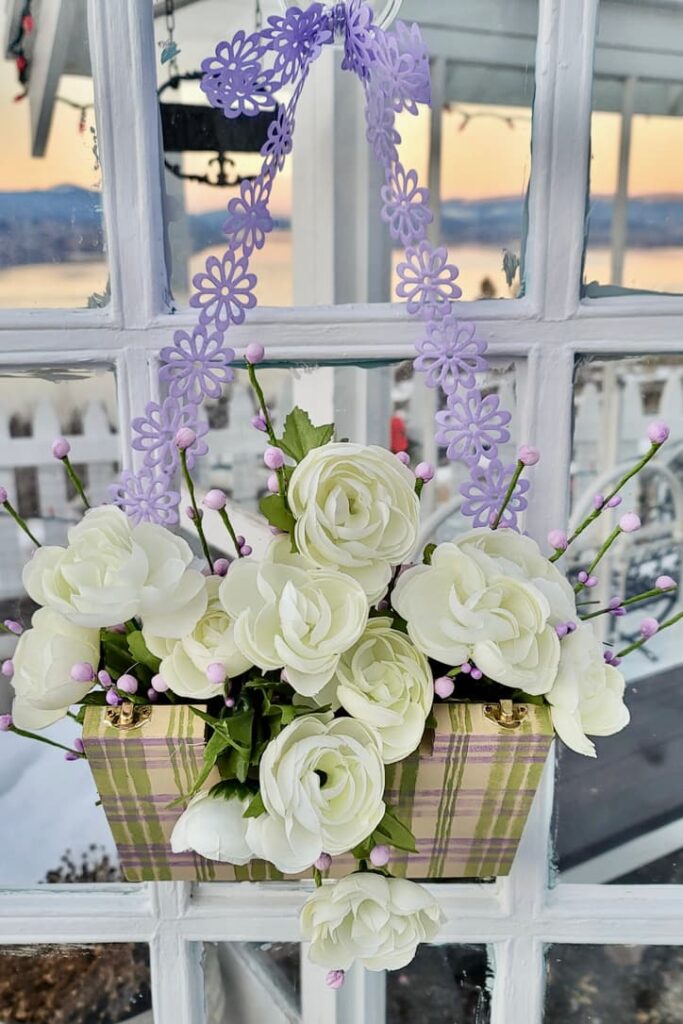 A wooden box filled with white flowers hanging on a purple ribbon on the front door
