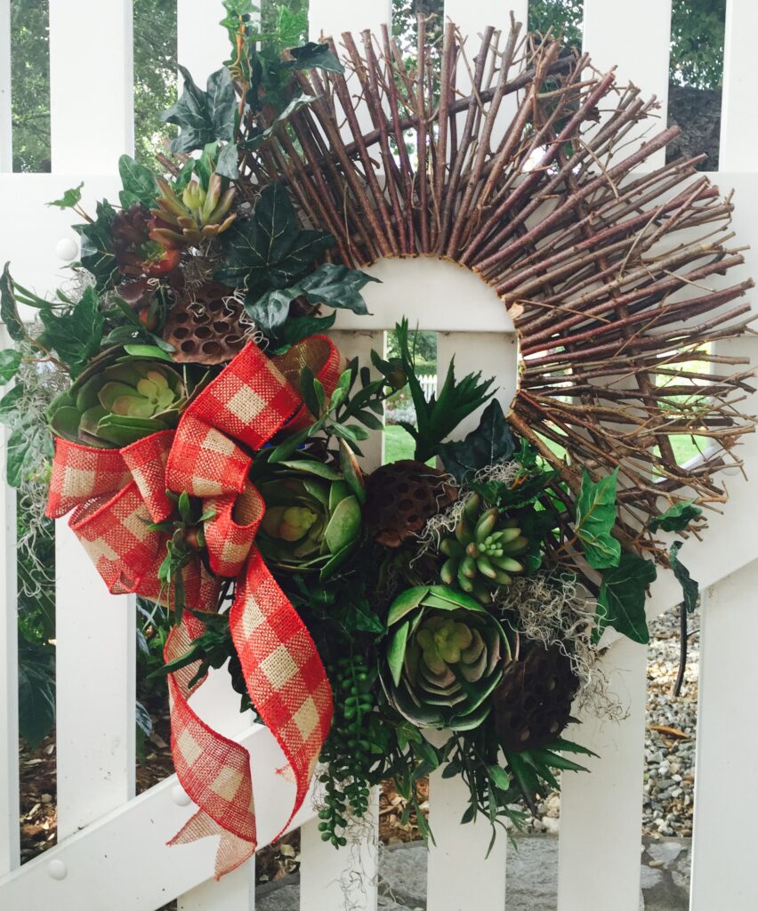 A twig wreath with faux succulents and a red and white ribbon attached.
