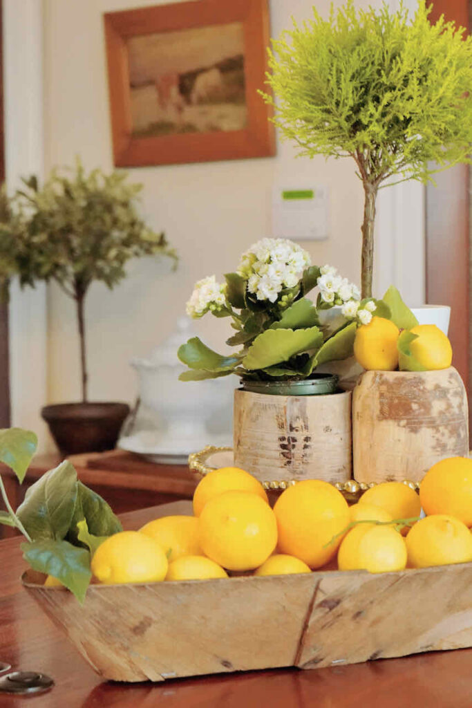 29 things to do with your extra lemons- lemons in a wooden bread form sitting on a kitchen counter with a cypress tree