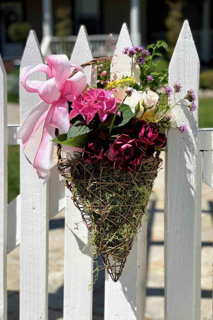 May Day basket full of flowers hanging on a fence. 