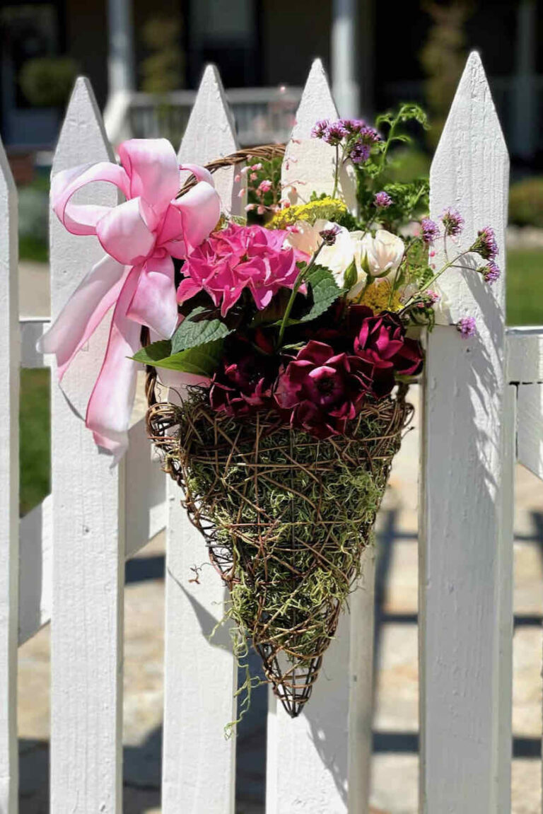 May Day basket full of flowers hanging on a fence.