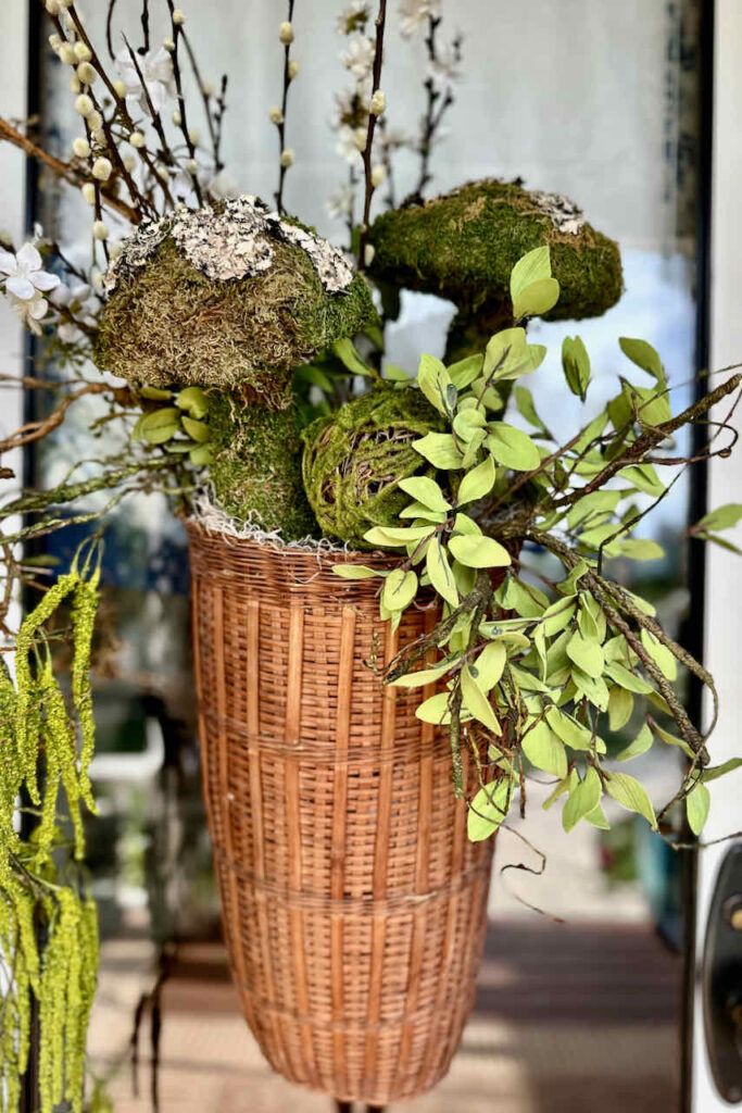 a basket hanging on the front door with faux greens and moss mushrooms