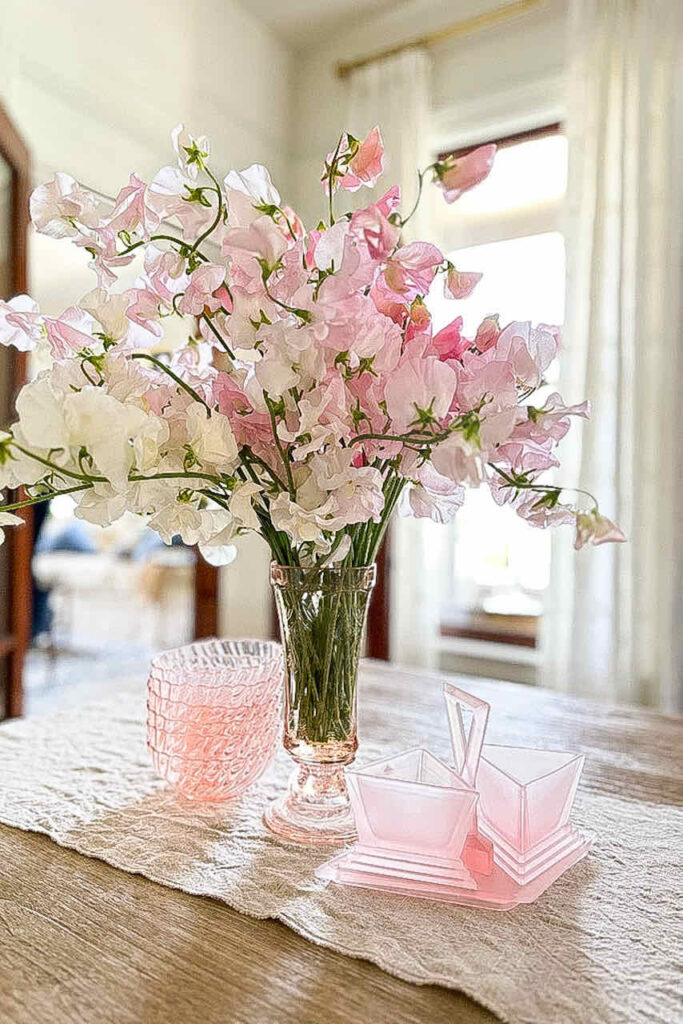 The Best Quick and Easy Sweet Pea Floral Arrangement-Pastel shade of pink sweet peas fill a clear glass vase sitting on a dining room table with pink glassware