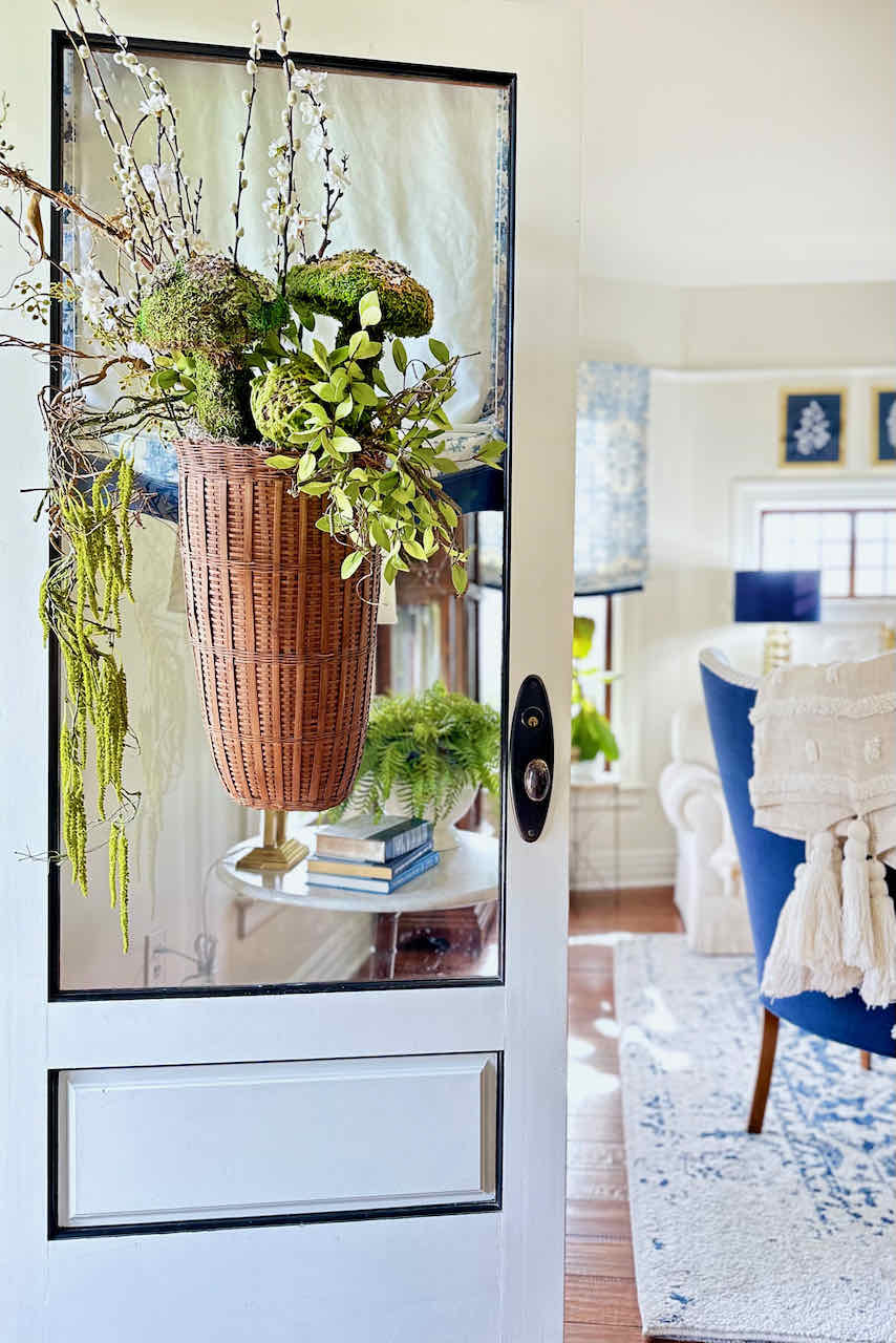 How To Make 27 Unique Summer Front Door wreaths And More- a vintage wicker basket hanging on the front door, filled with greenery, moss and moss mushrooms. 