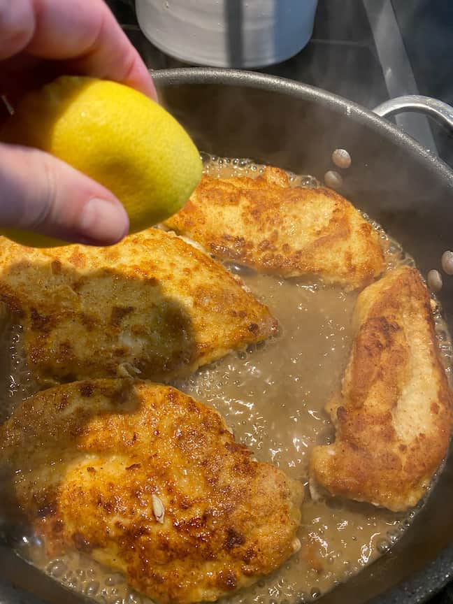 emon chicken cooking in the skillet. lady squeezing lemon on the chicken as well. 