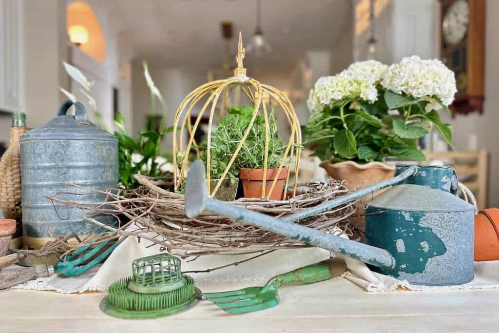 Kitchen table decorated with vintage garden decor interior- watering can, clay pots, floral frogs and more. 