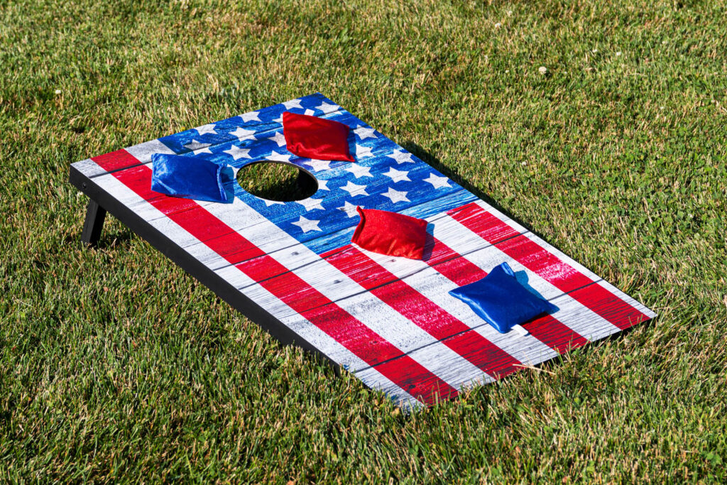 Corn hol board that looks like an Amerian flag with 2 red and 2 blue bean bags sitting on the grass.