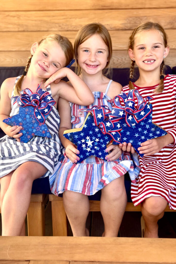 Three girls dressed for Memorial day showing off their decopauged stars they made at the craft table.