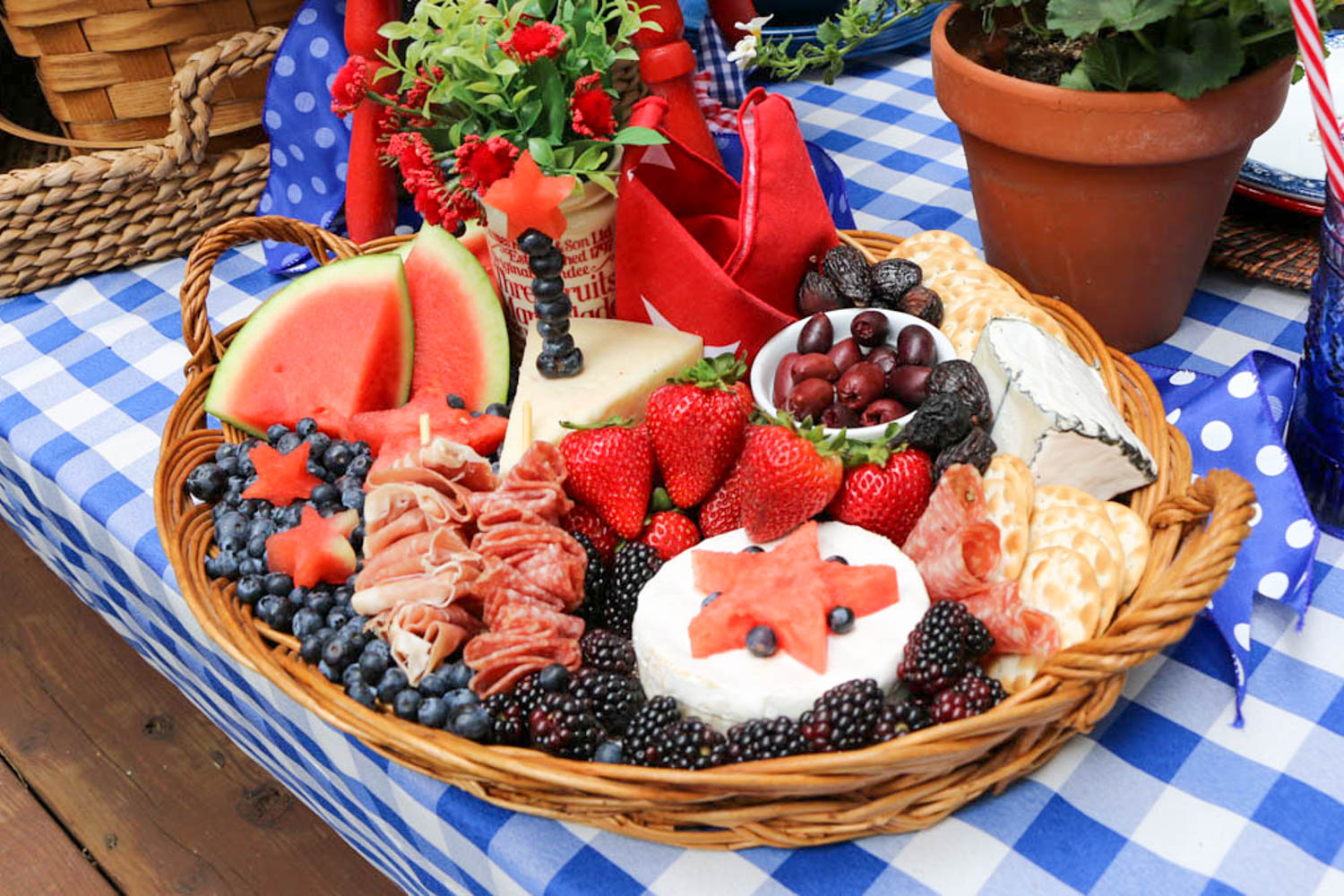 Memorial Day Party Ideas- Charcuterie basket filled with blueberries, boysenberries, brie cheese, strawberries, olives, and watermelon cut in the shape of stars.
