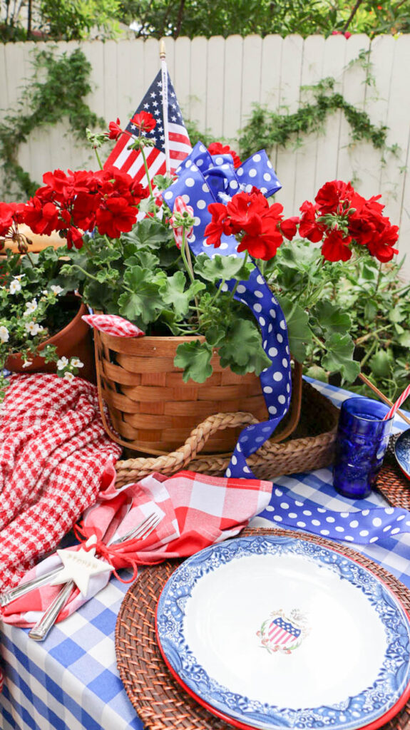 Memorial Day Party Ideas- A table decorated fora the party with re,d white, and blue. I checkered table cloth with a picnic basket filled with red geraniums.