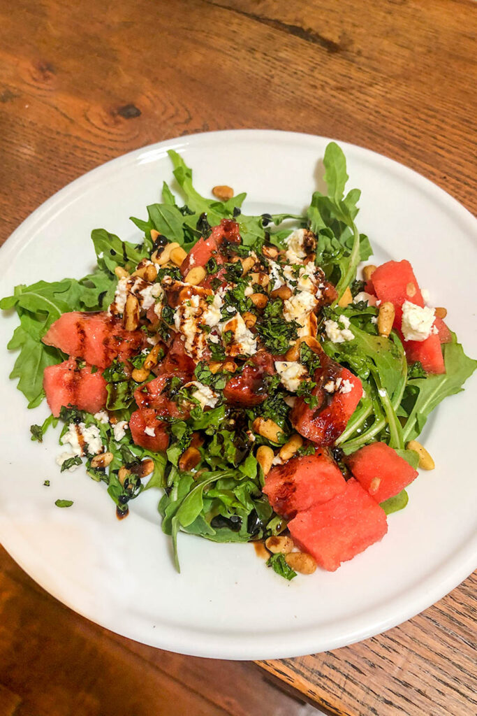 Arugula salad on a white plate with feta cheese, watermelon and balsalmic dressing 