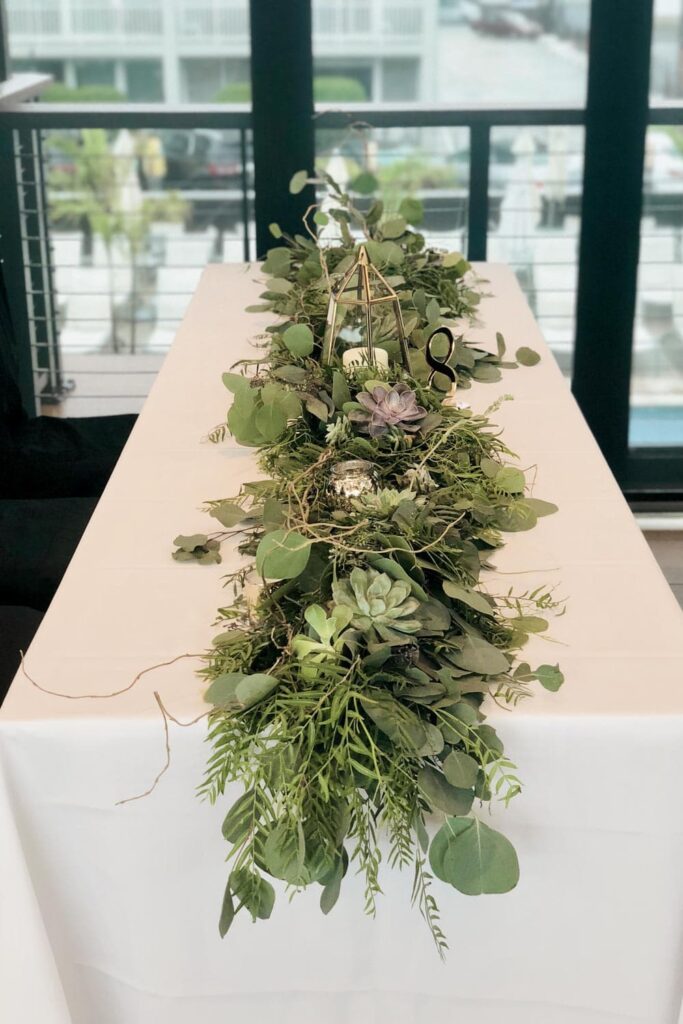 How to use succulents in beautiful floral arrangements- a table at a wedding reception with green garland and succulents down the center.