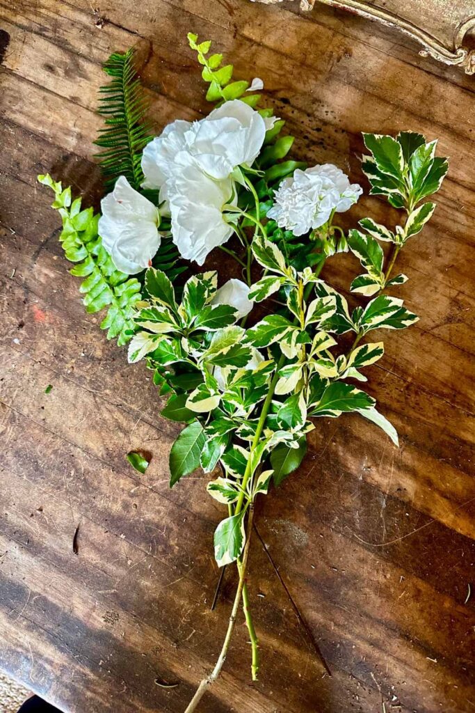how to use succulents to arrange with flowers - fern, white roses laying on a table to make a bouquet