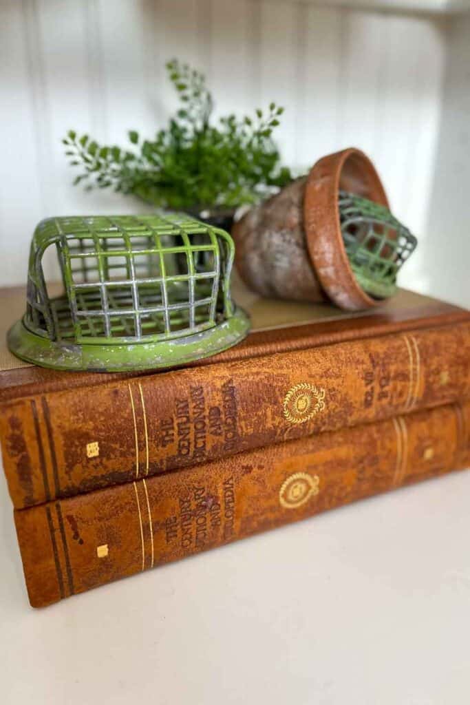 Vintage books with an old floral frog on top along with a terracotta pot and am smaller floral frog. 