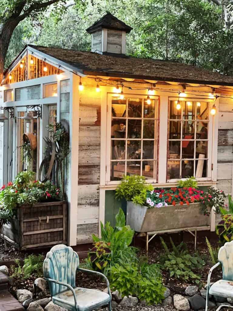 Vintage garden decor Indoors- Vintage She Shed made of old windows and doors lit up with market lights in the evening