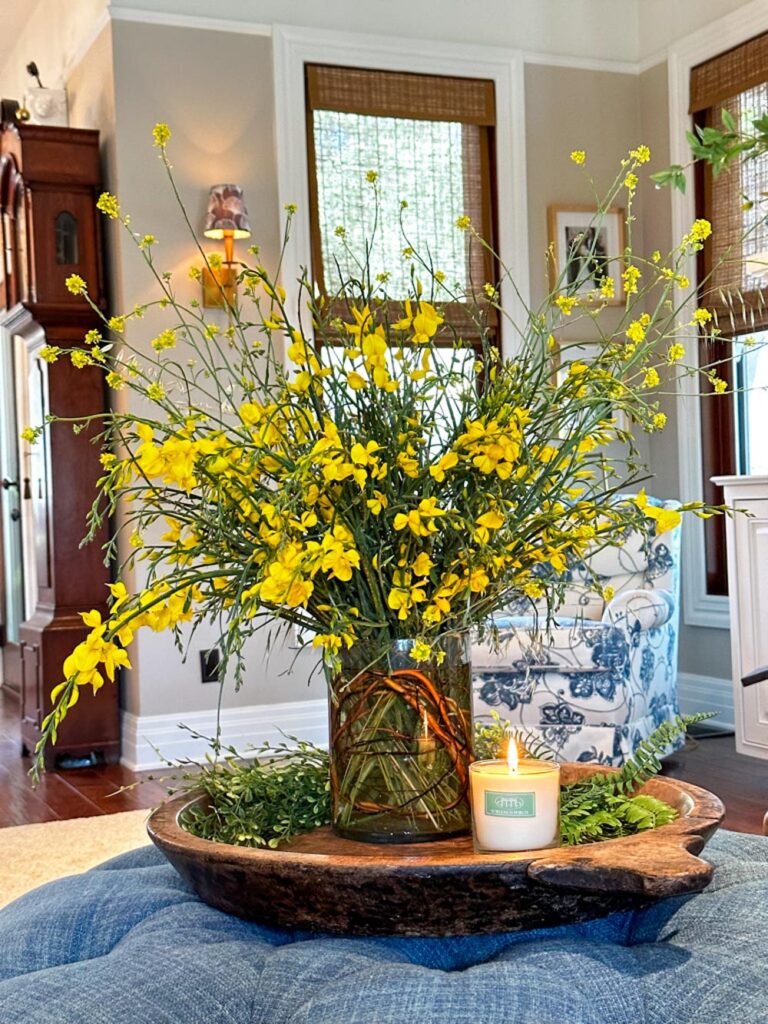 DIY wildflower floral arrangement of Spanish broom in bright yellow sitting on a wood tray with a lit candle on a blue ottoman