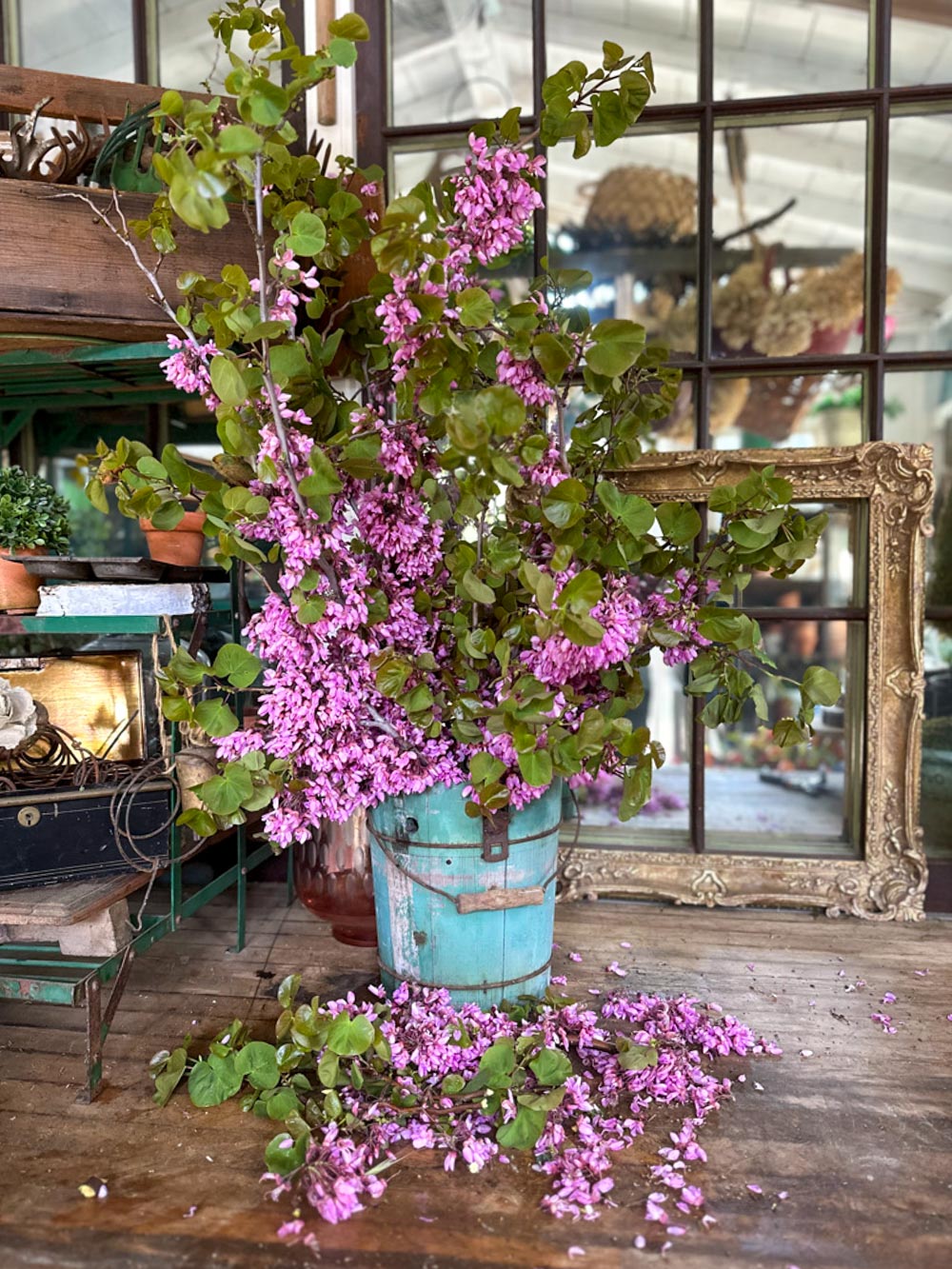 Wildflower floral arrangement of red buds in a blueish green bucket with petals falling to the ground