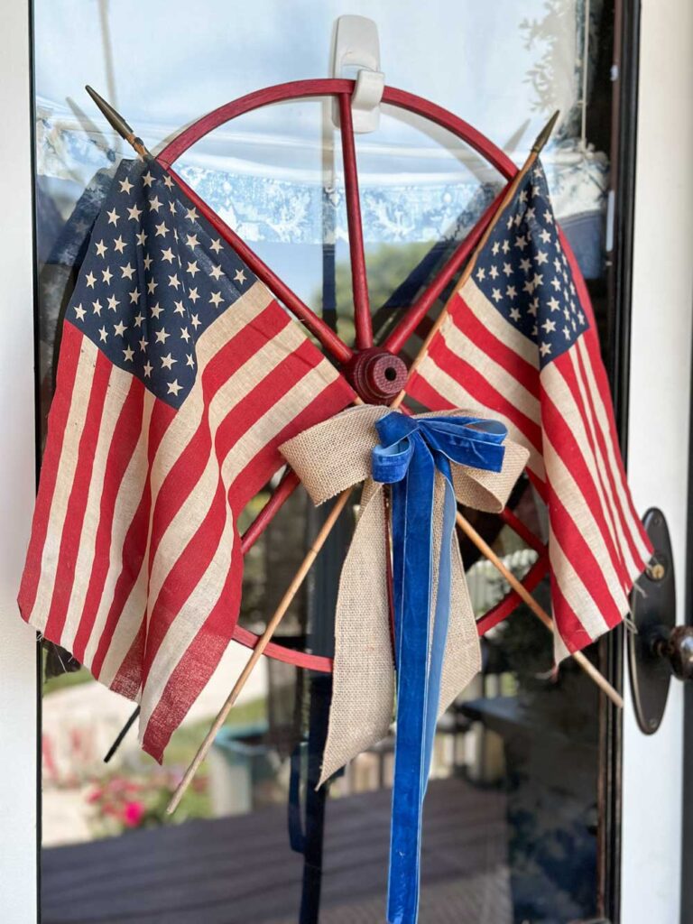 The Best DIY Wagon Wheel Wreath With Dollar Tree Ribbon-wagon wheel wreath on the front door with two American flags for the fourth of July