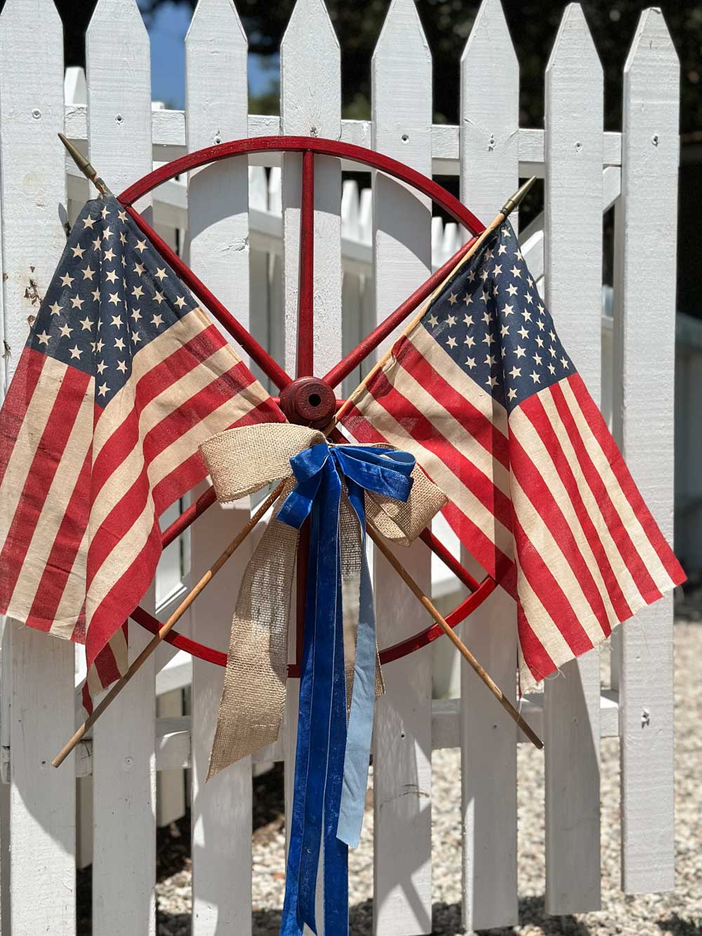 4th of July wagon wheel wreath hangin on a white picket fence gate