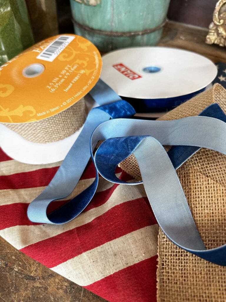 DIY Wagon Wheel Wreath- ribbon, flags and wagon wheel sitting on a table before being assembled 