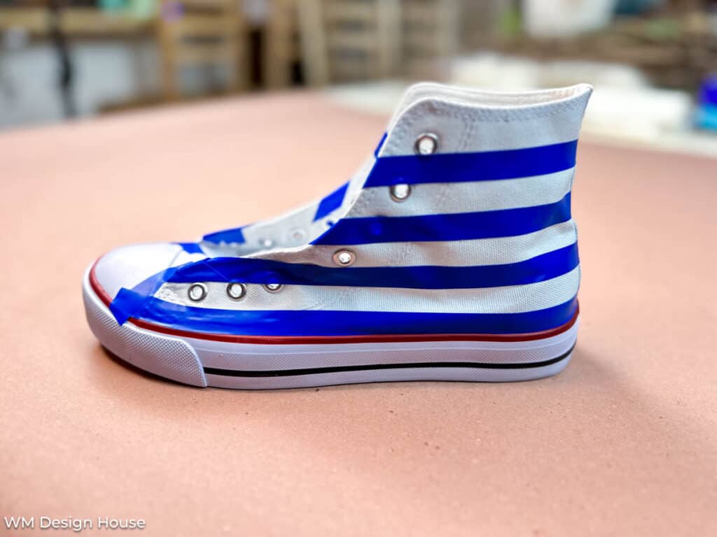 how to paint a canvas shoe- a shoe with taped off stripes on the side in preperation for painting 