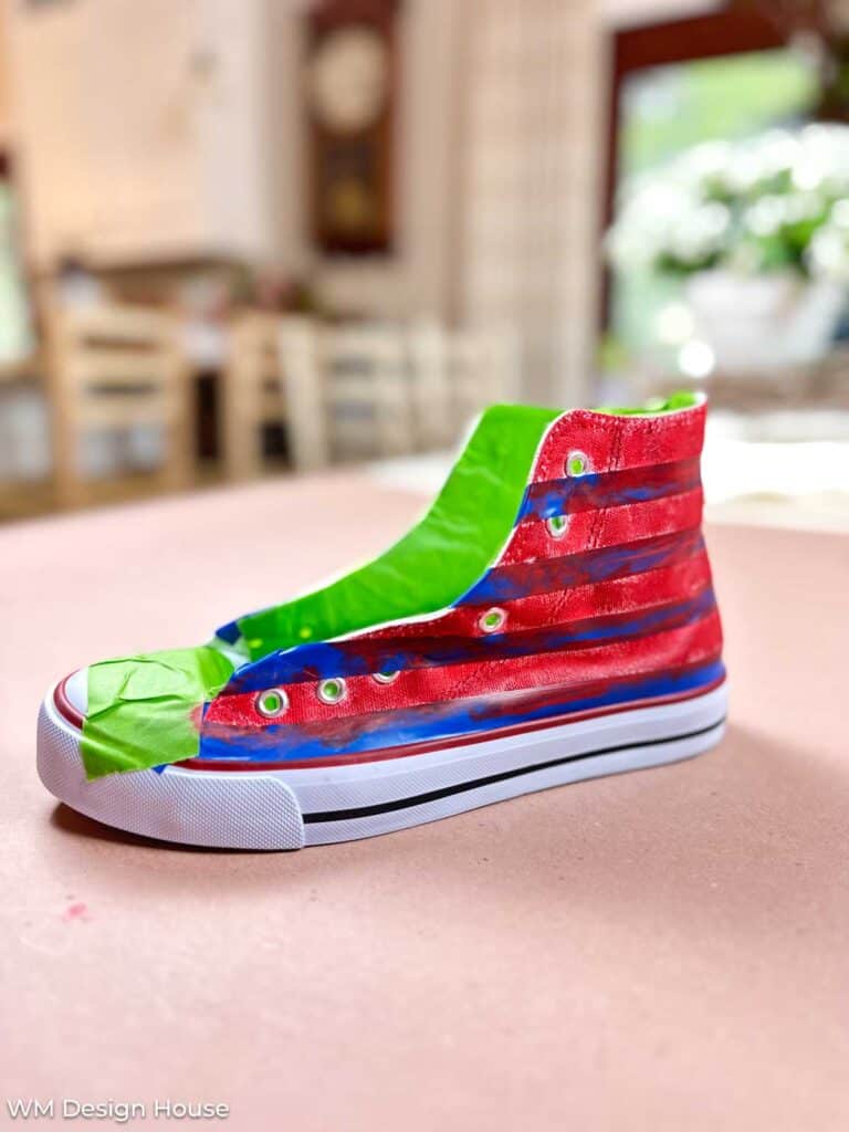 How to paint canvas shoes - a white high top tennis shoe with tape marking off the stripes that are painted red